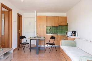 A compact living space with a kitchenette, a dining area with two chairs, and a sofa. - Le Refuge de Rena - Appart Climatisé (San-Nicolao)