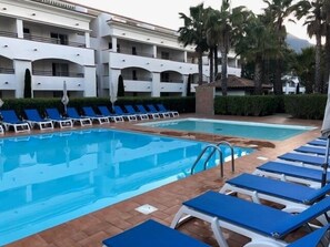 A swimming pool with blue lounge chairs and a building with balconies in the background. - Le Refuge de Rena - Appart Climatisé (San-Nicolao)