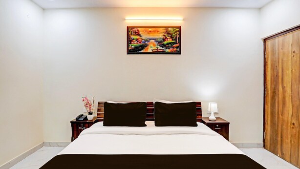 A hotel room with a large bed, two bedside tables, a nightstand, a wooden wardrobe, and a painting on the wall. - Classic Lucknow Inn (Lucknow)