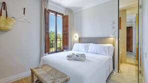 Ein Hotelzimmer mit Bett, einer Bank, einem fenster mit Vorhängen, einer hängenden Ampel und einem Spiegel.