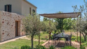 Eine Terrassenfläche mit Tisch und Stühlen, umgeben von einem Garten mit verschiedenen Pflanzen und einem Gebäude mit Steinverkleidung.