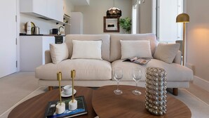 Un salon moderne avec un canapé beige, une table basse sur laquelle se trouvent un livre et une télécommande, et un vase décoratif.