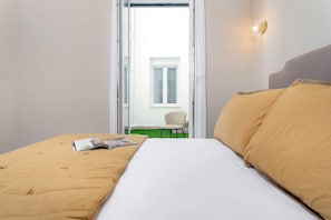 Ein Hotelzimmer mit einem Bett, einer Zeitschrift auf dem Bett, einem Stuhl vor der Tür und Blick auf ein Gebäude.