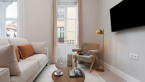 A modern living room with a sofa, a coffee table, a chair, a TV mounted on the wall, and a window with curtains. - Genteel Home San Anton 101 (Granada)