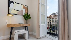 A modern living room with a wooden desk, a small stool, a potted plant, and a large window with a view of the city. - Genteel Home San Anton 101 (Granada)