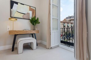 A modern living room with a wooden desk, a small stool, a potted plant, and a large window with a view of the city. - Genteel Home San Anton 101 (Granada)