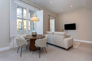 A modern living room with a sofa, a dining table with chairs, a TV mounted on the wall, and large windows with curtains. - Genteel Home San Anton 101 (Granada)
