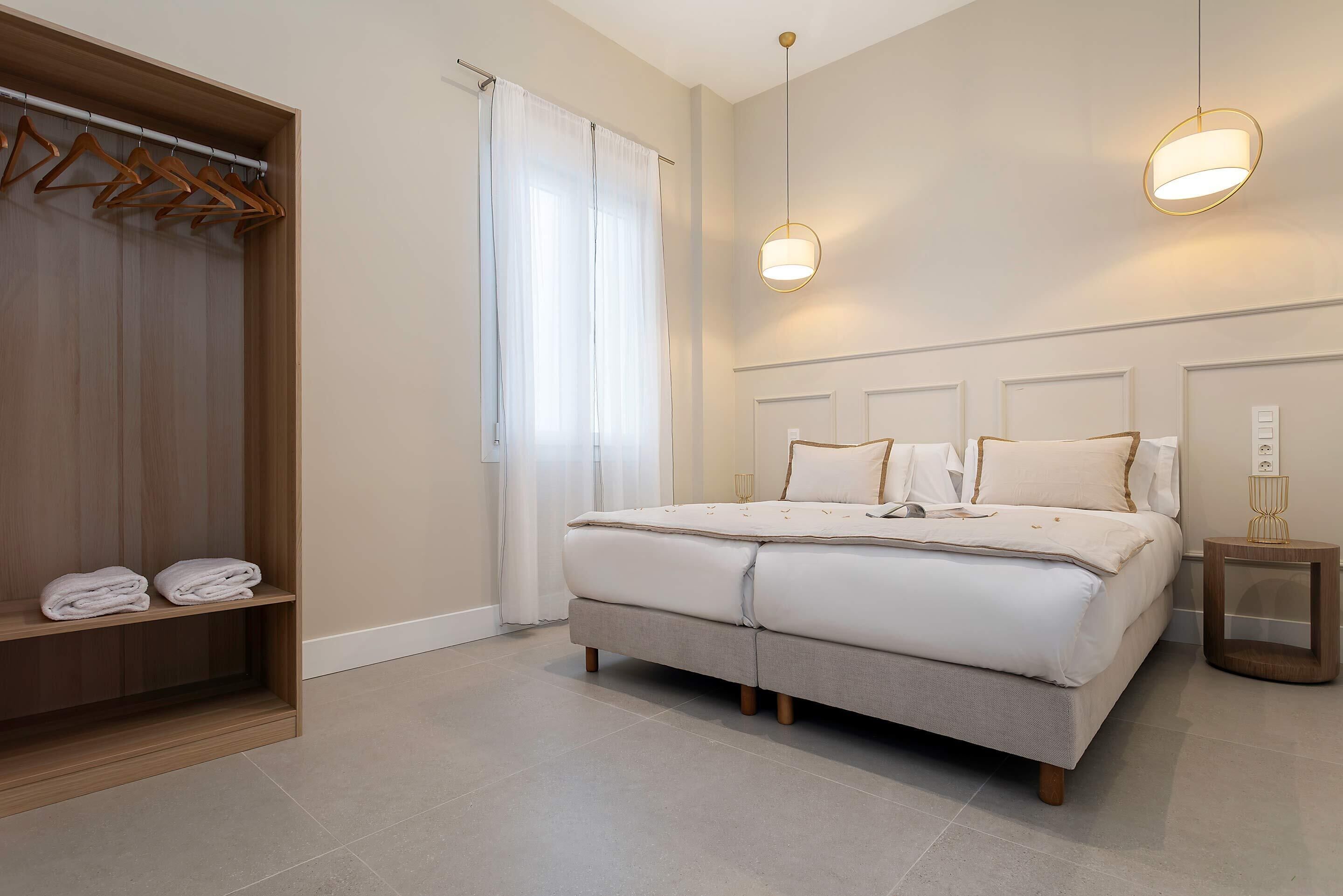 Quarto com cama, mesas de cabeceira, guarda-roupa e janela com cortinas.