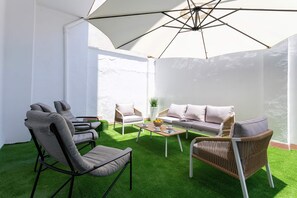 An outdoor seating area with a white umbrella, a wicker chair, a sofa, and a coffee table. - Genteel Home San Anton 102 (Granada)