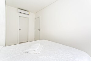 A hotel room with a neatly made bed, a white air conditioning unit, and two white doors. - Apt in Building w/ Pool 350m From the Beach Rtg208 (Florianópolis)