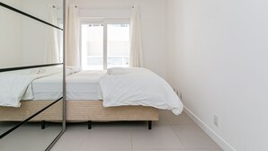 Een slaapkamer met een bed, een raam met gordijnen en een spiegel.