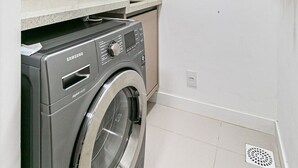 Een kleine wasruimte met een Samsung wasmachine, een wasbak en een boiler.