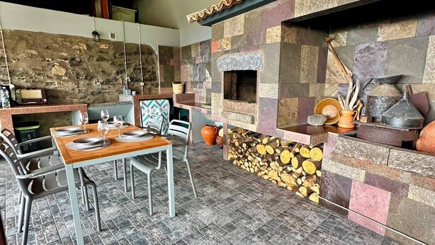 An outdoor dining area with a stone fireplace, wooden ceiling, and tiled flooring. - Jade's House BBQ & Sea View Villa (Calheta)