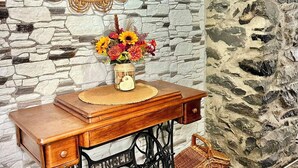A vintage Singer sewing machine with a wooden table, a decorative mirror, and a vase with flowers against a stone wall backdrop. - Jade's House BBQ & Sea View Villa (Calheta)