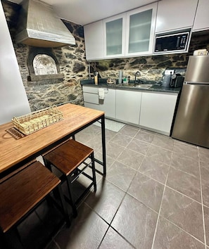 Une cuisine avec un mur de crédence en pierre, des armoires blanches, des appareils électroménagers en acier inoxydable et une table à manger en bois.