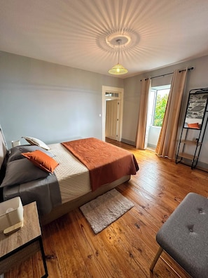A bedroom with a bed, a desk, a chair, a wardrobe, and a window with curtains.