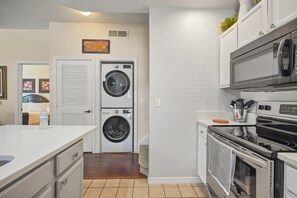 A compact kitchen with a microwave, oven, and stacked washer-dryer unit. - Cozy Kissimmee Getaway Near Orlando Attractions (Kissimmee)