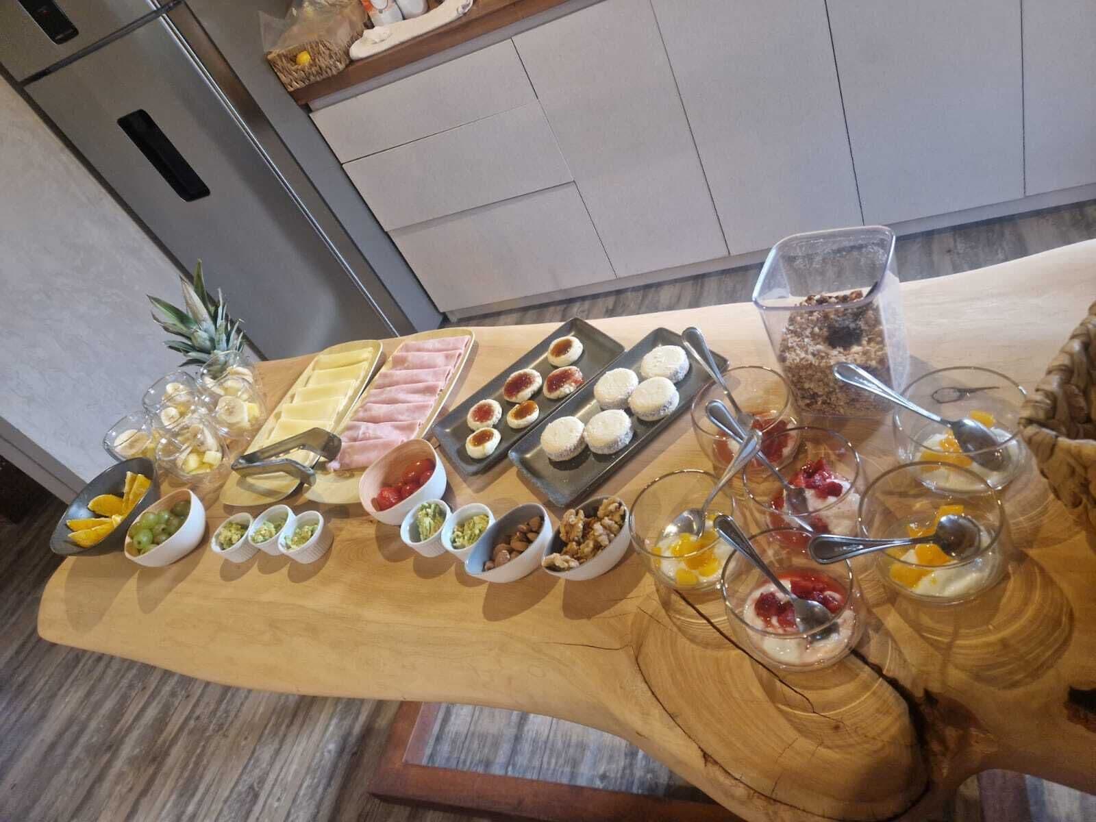 Una mesa de madera con diversas opciones de comida y bebidas, como frutas, quesos y postres.