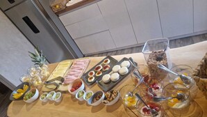 Une table en bois sur laquelle sont disposés divers aliments et boissons, notamment des fruits, des fromages et des desserts.