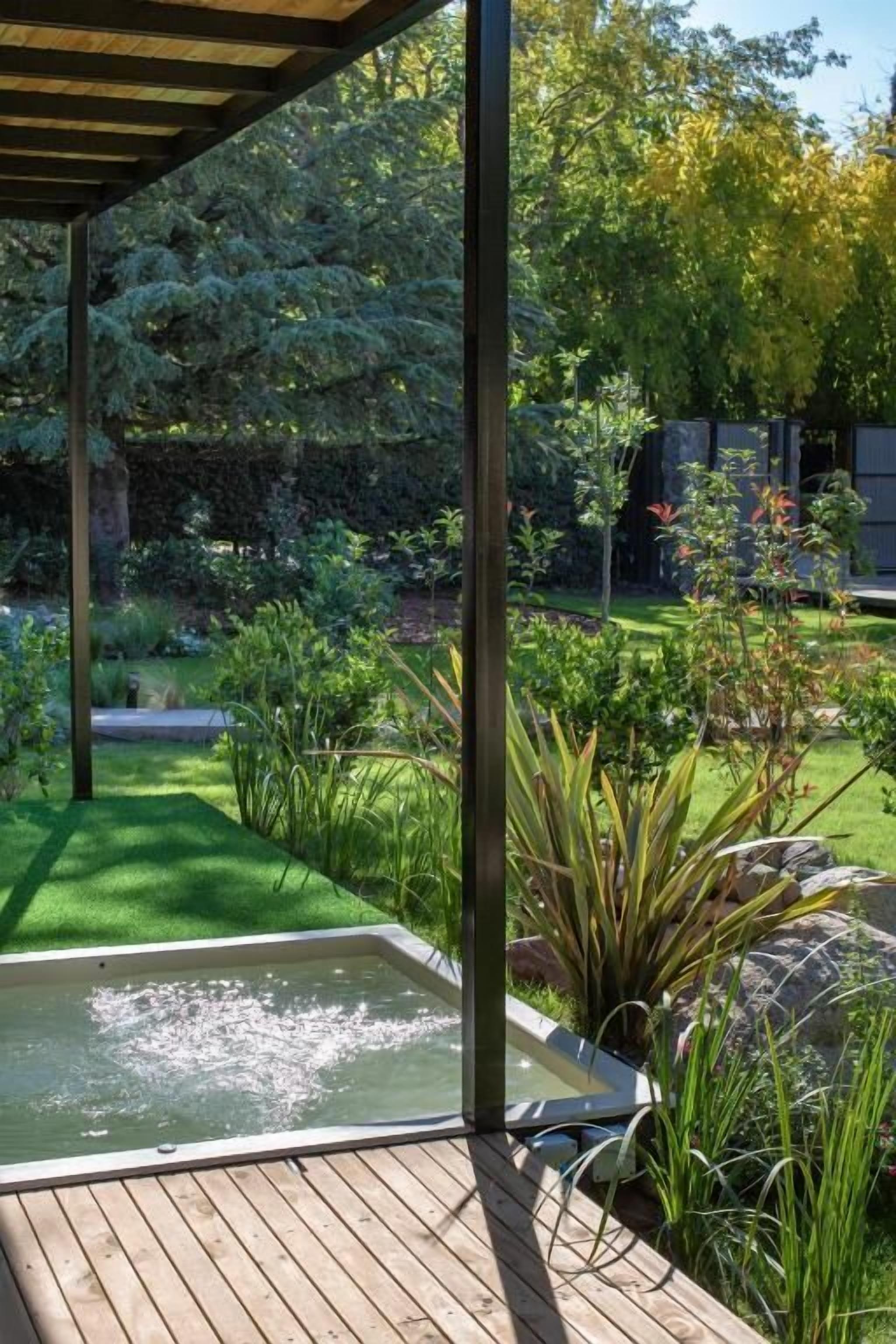Una terraza de madera con un jacuzzi, rodeada de exuberante follaje y un jardín.