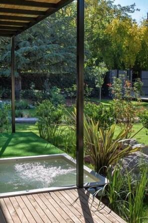 A wooden deck with a hot tub, surrounded by lush greenery and a garden.