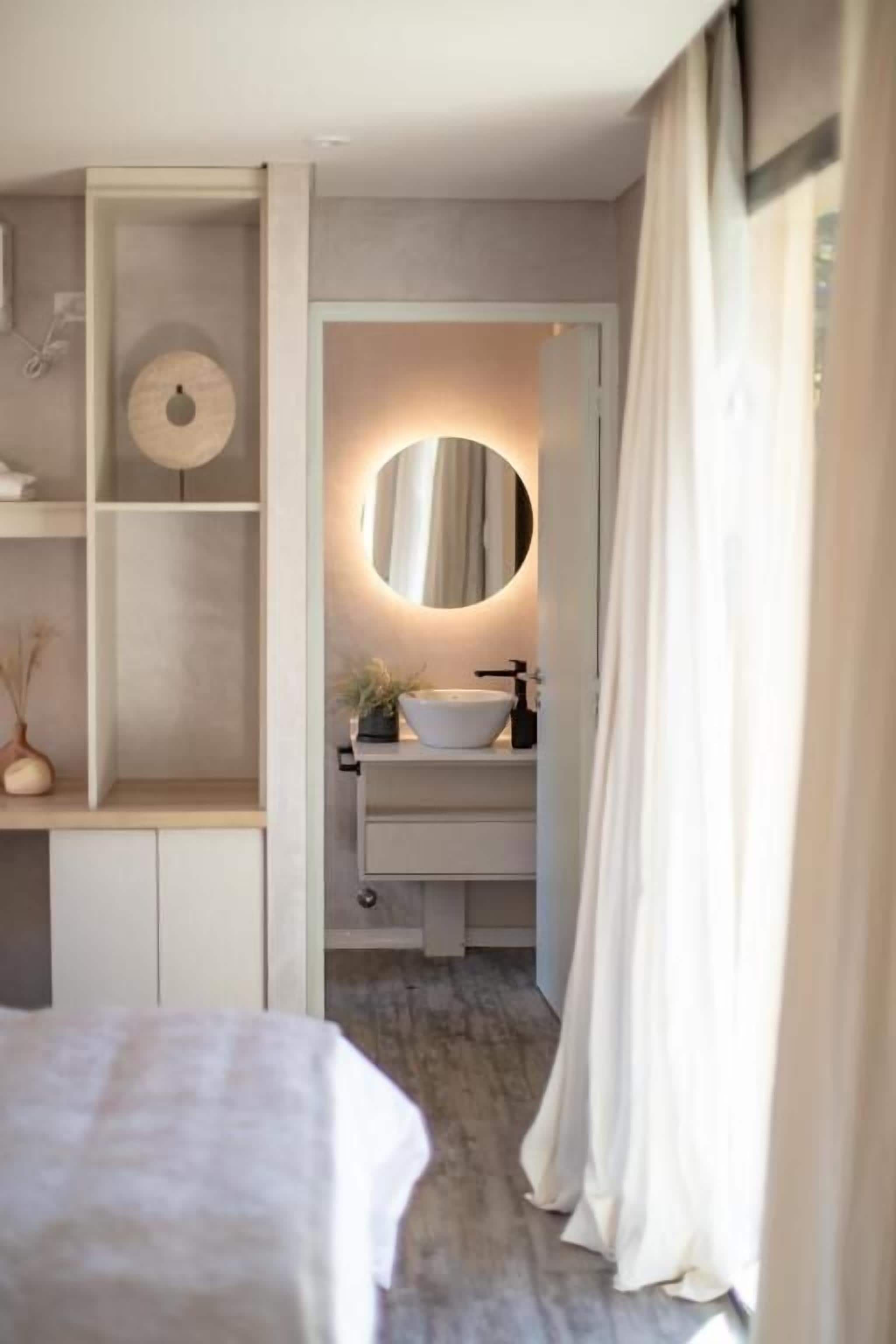 Un dormitorio con cama, mesita de noche y repisa empotrada, espejo y una pequeña planta.