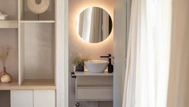 Une chambre à coucher comprenant un lit, une table de chevet, une commode et une étagère intégrée agrémentée d’un miroir et d’une petite plante.
