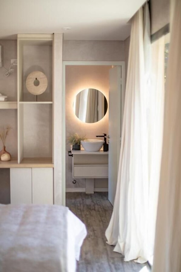 A bedroom with a bed, a bedside table, a nightstand, and a built-in shelf with a mirror and a small plant.