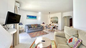 Ein Wohnzimmer mit Fernseher, Sofa, Couchtisch und einem Essbereich mit Tisch und Stühlen.