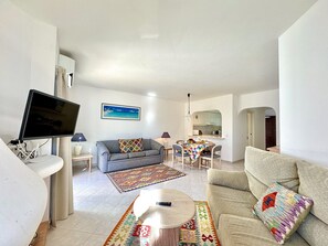Ein Wohnzimmer mit Fernseher, Sofa, Couchtisch und einem Essbereich mit Tisch und Stühlen.