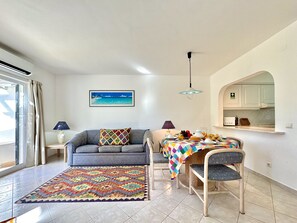 Ein Wohnzimmer mit Sofa, einem Couchtisch mit Speisen, einem Teppich und einem Strandbild.