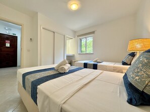 Ein Hotelzimmer mit zwei Betten, einem Fenster, einer Lampe und einer Tür.