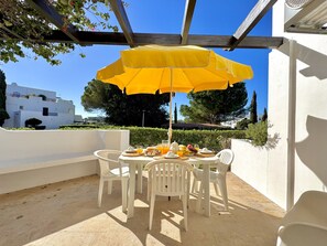 Eine Terrasse mit Tisch, Stühlen und einem gelben Sonnenschirm.