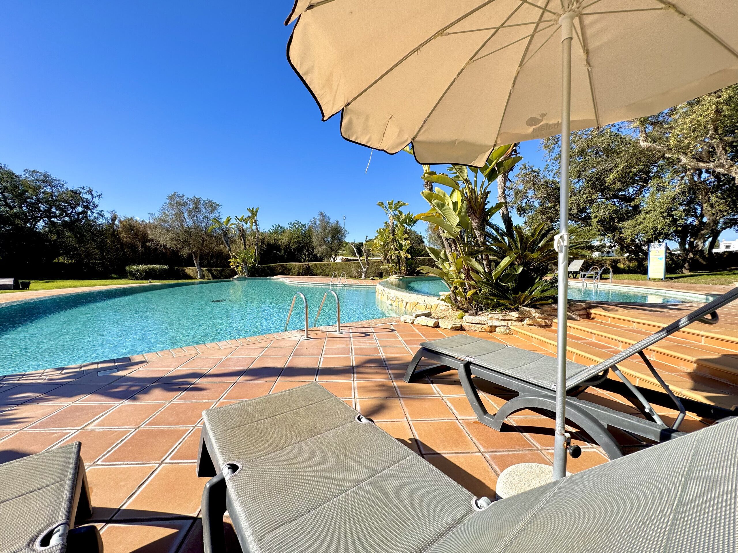 Une piscine avec un revêtement de sol en carrelage, des chaises longues et un parasol.