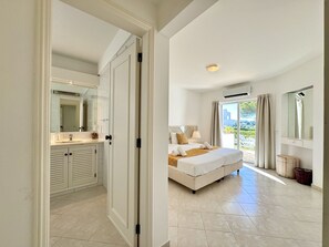 Une chambre avec un grand lit, une salle de bain avec un miroir et un lavabo, et une vue sur l’extérieur grâce à une porte vitrée.