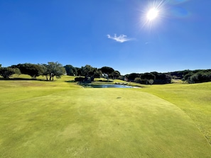 Ein Golfplatz mit Teich, Bäumen und blauem Himmel.