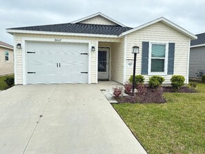 Einbungalow mit Garage, Eingangstür und kleinem Vorgarten mit Sträuchern.