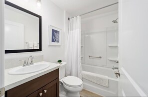 Une salle de bain avec un lavabo blanc, des toilettes, une douche avec une porte en verre et un tableau encadré au mur.