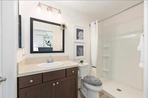 Une salle de bain comprenant un lavabo, un miroir, un tableau encadré, des toilettes, une douche et un porte-serviettes.