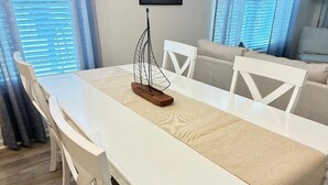 Un tavolo da pranzo con un centrotavola a forma di vela, circondato da sedie bianche, in una stanza con una finestra e tende.