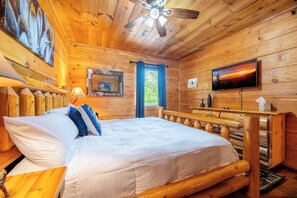 Une chambre dans un chalet en bois, équipée d’un lit, d’une télévision et d’un ventilateur de plafond.