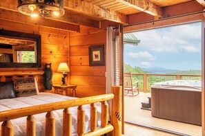 A wooden cabin interior with a bed, a lamp, a framed picture, and a hot tub on an outdoor deck. - Big Bear Lodge - 7BR Mtn Retreat, Theater & Hot Tub (Sevierville)