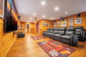 Een gezellige kamer met houten inrichting, een grote flatscreen televisie aan de muur, een zithoek met leren fauteuils, en een deur die naar een andere kamer leidt.