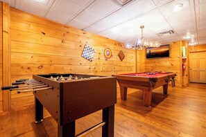 A wooden-floored room with a foosball table, pool table, and a television mounted on the wall. - Big Bear Lodge - 7BR Mtn Retreat, Theater & Hot Tub (Sevierville)