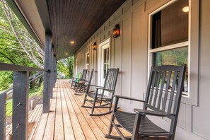 A wooden deck with rocking chairs and a covered area with windows. - Little River | Hot Tub + Games & Great Location (Walland)