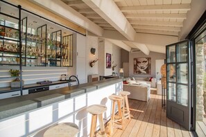 A modern kitchen with a bar area, wooden stools, and a large window. - Vue imprenable, à 5 min à pied du village. (Saint-Rémy-de-Provence)