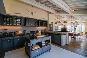 A modern kitchen with dark cabinetry, a central island, and a hanging light fixture. - Vue imprenable, à 5 min à pied du village. (Saint-Rémy-de-Provence)