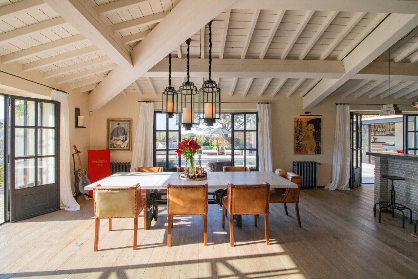 Un espace repas doté d’un plafond haut et de poutres apparentes, une table avec des chaises et une vue sur l’extérieur.
