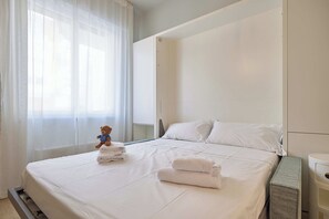 A neatly made bed with white linens, a teddy bear, and folded towels. - Mare e Conchiglie - Studio Apartment, Sleeps 2 (Albenga)