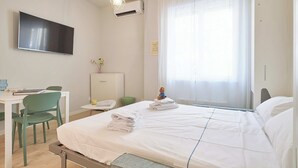 Ett hotellrum med en säng, ett skrivbord med en stol, en tv och ett fönster med gardiner.